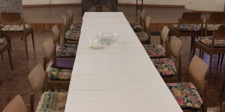 Kirchenraum mit Altar und Kreuz im Hintergrund, im Vordergrund Tisch mit Stühlen und weißen Tischdecken